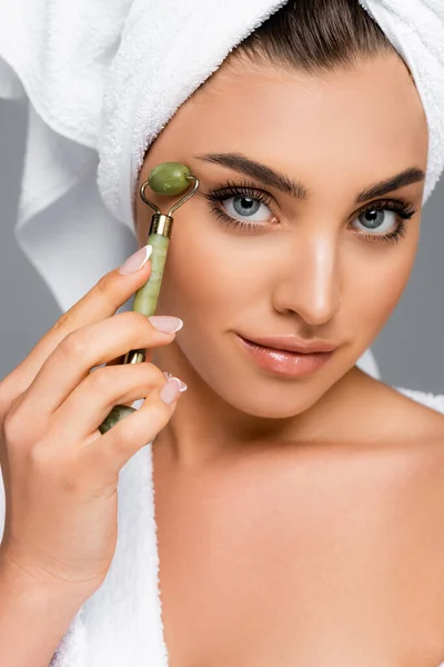 Femme avec serviette sur la tête à l'aide d'un rouleau de jade sur le visage isolé sur gris — Photo de stock