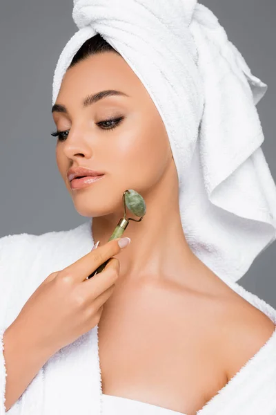 Woman with towel on head using jade roller on face isolated on grey — Stock Photo