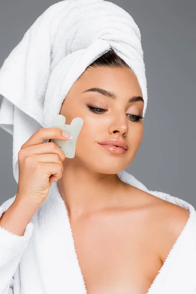 Femme avec serviette sur la tête en utilisant gua sha sur le visage isolé sur gris — Photo de stock