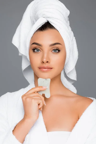Donna con asciugamano sulla testa utilizzando gua sha sul viso isolato sul grigio — Foto stock