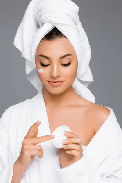 Woman with towel on head and cosmetic cream on face holding container isolated on grey — Stock Photo