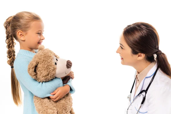 Pediatra sonriente mirando a chica con juguete suave aislado en blanco - foto de stock