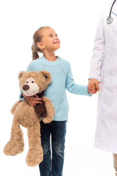 Fille avec jouet doux tenant la main et souriant au pédiatre isolé sur blanc — Photo de stock