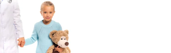 Panoramic crop of girl holding teddy bear and hand of doctor isolated on white — Stock Photo
