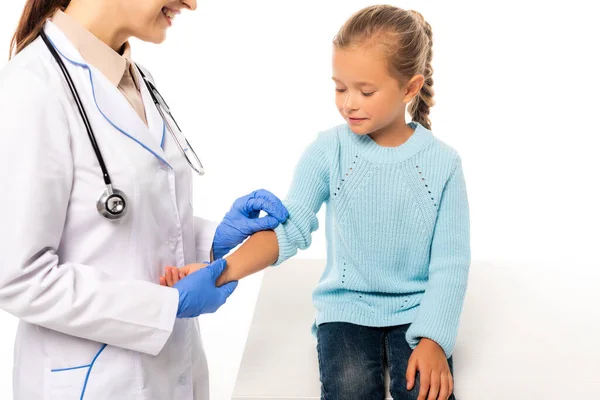 Médico sonriente con guantes de látex tomados de la mano de un niño aislado en blanco - foto de stock