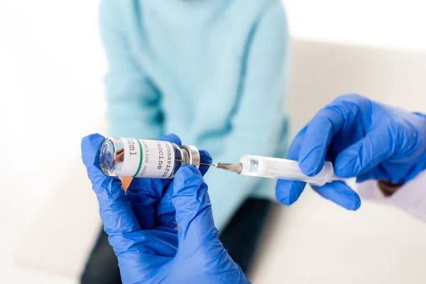 Обрізаний вид лікаря, який збирає вакцину проти коронавірусу в шприці біля дитини ізольовано на білому — стокове фото
