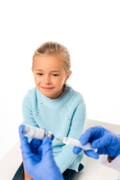Selektiver Fokus des lächelnden Mädchens auf den Kinderarzt, der Spritze und Impfstoff auf Weiß isoliert hält — Stockfoto