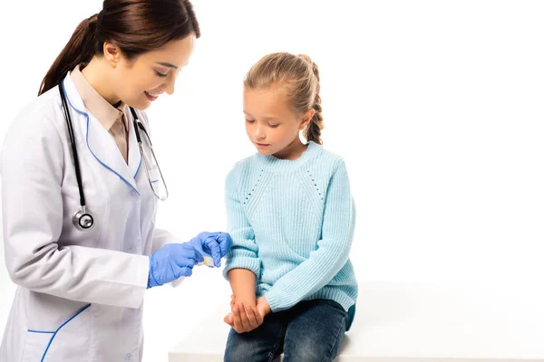 Pediatra sonriente sosteniendo parche cerca de la mano del niño aislado en blanco - foto de stock