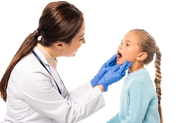 Enfoque selectivo del pediatra sonriente en guantes de látex mirando a una chica con la boca abierta aislada en blanco - foto de stock