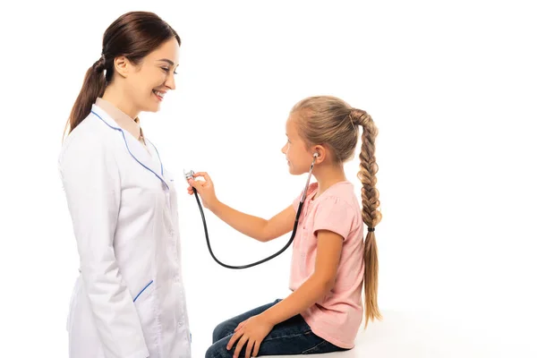 Child holding stethoscope near smiling doctor isolated on white — Stock Photo