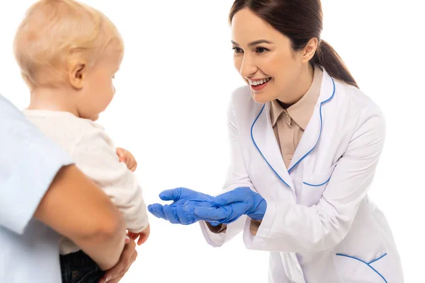 Selektiver Fokus des lächelnden Kinderarztes in Latexhandschuhen, der den Jungen in der Nähe des Vaters isoliert auf Weiß betrachtet — Stockfoto