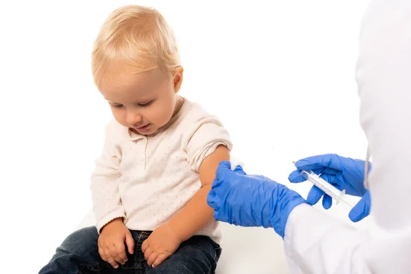 Enfoque selectivo del médico en guantes de látex que sostienen la jeringa cerca del niño pequeño aislado en blanco - foto de stock