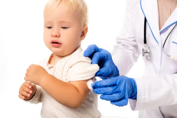 Selective focus of pediatrician in latex gloves holding cotton near hand of toddler isolated on white — Stock Photo