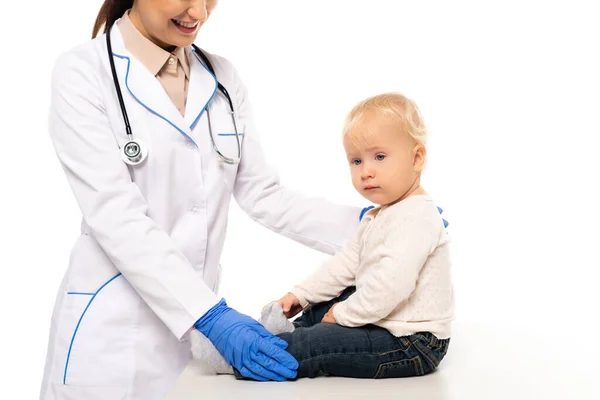 Smiling pediatrician touching toddler bot on table isolated on white — Stock Photo