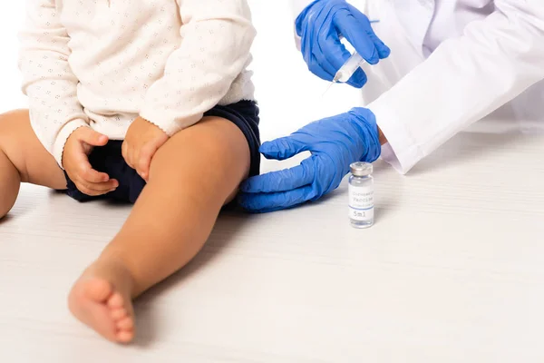 Vista ritagliata del pediatra che tiene la siringa vicino al vaccino e del bambino isolato su bianco — Foto stock