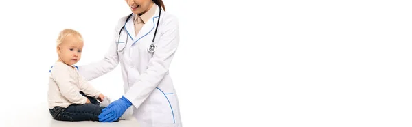 Panoramic shot of smiling pediatrician in white coat touching toddler boy isolated on white — Stock Photo
