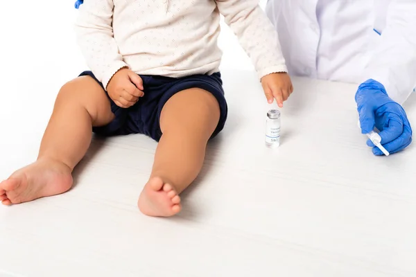 Vista ritagliata del medico che tiene la siringa vicino al bambino e vaso con vaccino isolato su bianco — Foto stock