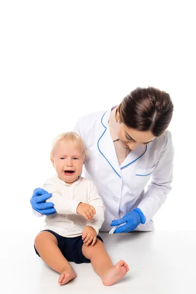 Лікар тримає шприц біля плачу малюка хлопчика ізольовано на білому — стокове фото