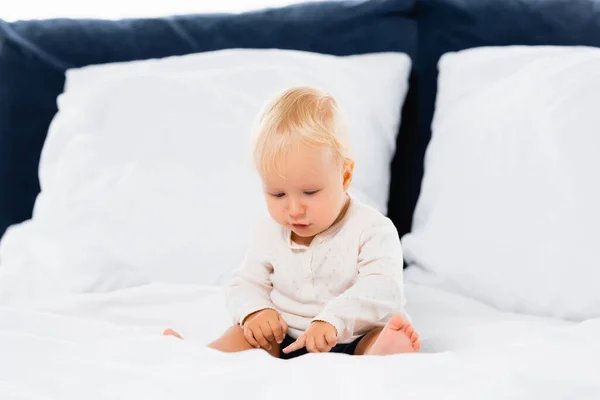 Kleinkind Junge zeigt mit dem Finger, während er auf dem Bett auf weißem Hintergrund sitzt — Stockfoto