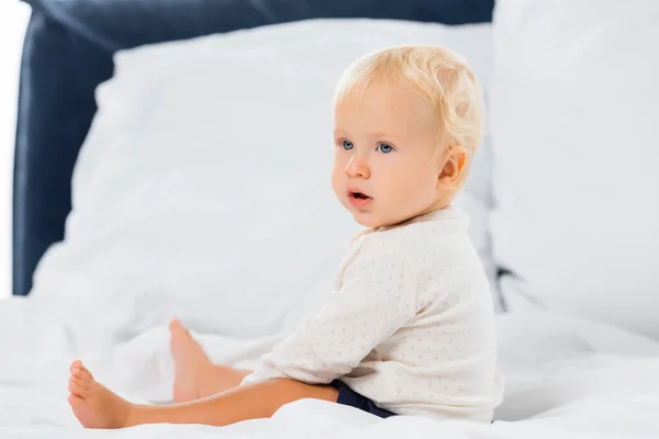 Вибірковий фокус хлопчика, який дивиться вбік, сидячи на ліжку на білому тлі — стокове фото
