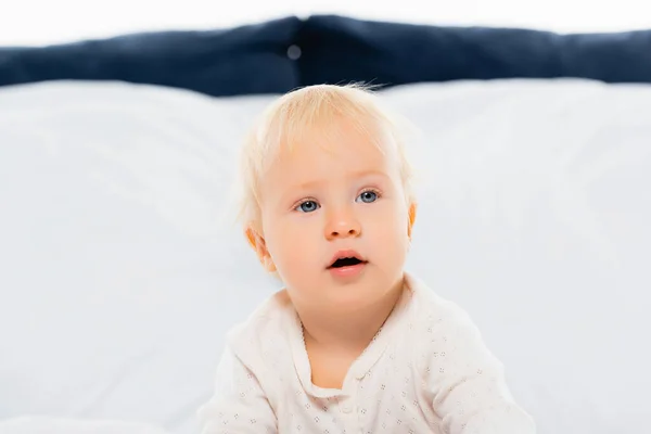 Блондинка малюк, дивлячись на ліжко на білому тлі — стокове фото