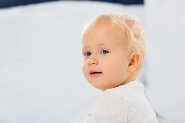 Focus selettivo del ragazzo bambino biondo che guarda lontano sul letto sul bianco — Foto stock