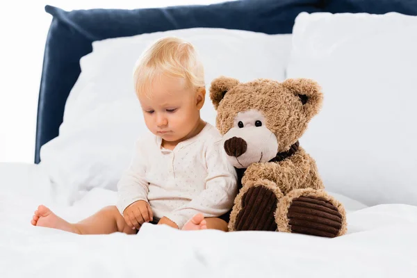 Selective focus of toddler sitting near soft toy on bed on white background — Stock Photo