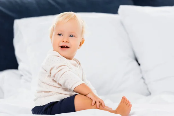 Selektiver Fokus des fröhlichen Kleinkindes, das auf dem Bett in die Kamera blickt — Stockfoto