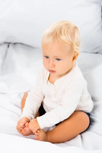 Focus selettivo del ragazzo bambino biondo seduto su biancheria da letto bianca — Foto stock