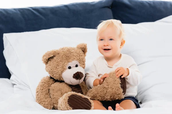 Foyer sélectif de tout-petit garçon souriant près de l'ours en peluche sur le lit sur fond blanc — Photo de stock