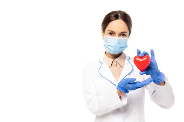 Médico en máscara médica y guantes de látex que sostiene el corazón aislado en blanco - foto de stock