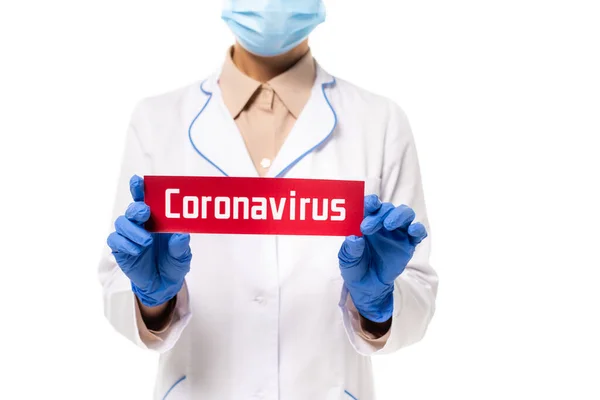 Обрізаний вид лікаря в медичній масці, що тримає картку з коронавірусом, записуючи ізольовані на білому — стокове фото