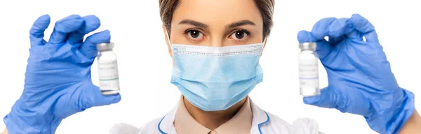 Panoramic shot of doctor in medical mask holding jars with vaccine isolated on white — Stock Photo