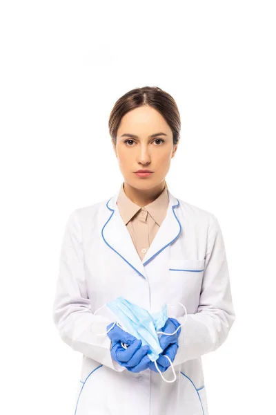 Médico en guantes de látex sosteniendo máscaras médicas y mirando a la cámara aislada en blanco - foto de stock