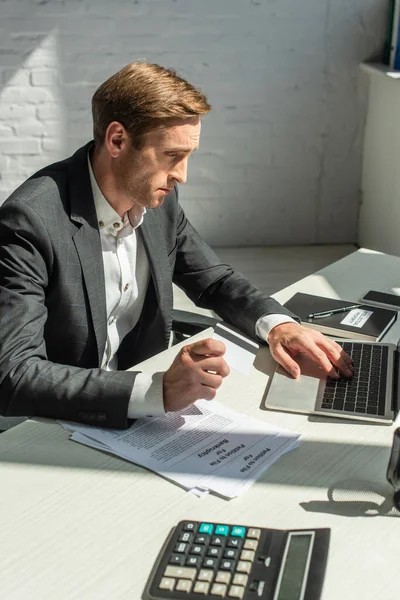 Disappointed businessman typing on laptop, while sitting near petitions for bankruptcy at workplace — Stock Photo