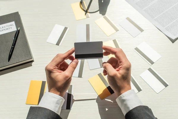 Vista cortada de empresário segurando cartão de crédito perto notebook e documento de negócios em fundo branco texturizado — Fotografia de Stock
