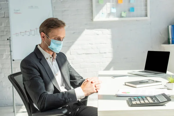 Businessman with clenched hands sitting on office chair at workplace with laptop and papers on table — Stock Photo