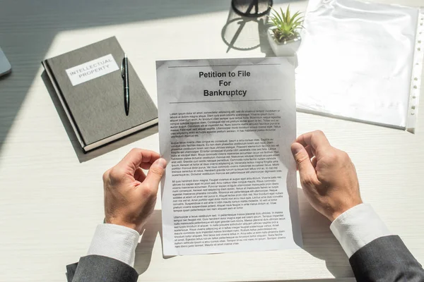 Cropped view of businessman holding petition for bankruptcy near notebook on white textured background — Stock Photo