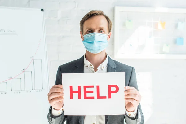 Front view of businessman holding sign with help lettering, while standing near flipchart on blurred background — Stock Photo
