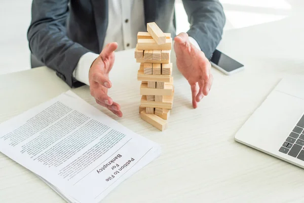 Cropped view of bankrupt with hands near blocks wood tower game, sitting at workplace — Stock Photo