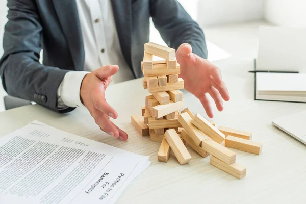 Cropped view of businessman with hands near blocks wood game falling, sitting near documents at workplace — Stock Photo