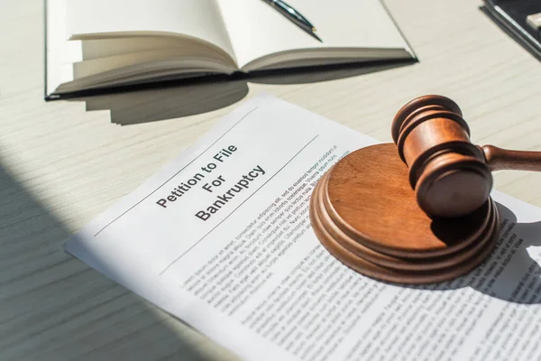 Wooden block with gavel on petition for bankruptcy near blank notebook on white textured background — Stock Photo