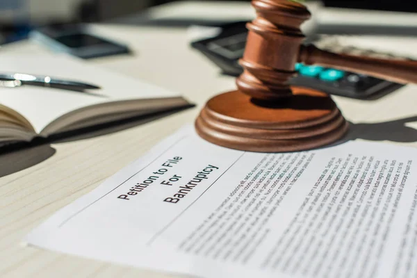 Close up view of gavel and wooden block on petition for bankruptcy on table with blurred stationery on background — Stock Photo