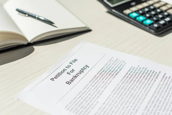 Vista de cerca de la petición de bancarrota con cuaderno borroso y calculadora sobre fondo texturizado blanco - foto de stock