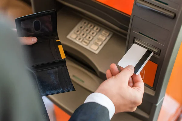 Vista recortada del hombre de negocios con cartera, poner la tarjeta de crédito en el cajero automático en primer plano borrosa - foto de stock