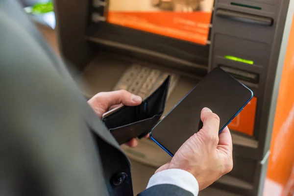 Cropped view of businessman with empty wallet, holding smartphone, while standing near atm on blurred foreground — Stock Photo