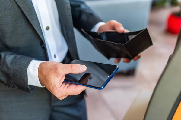 Vista recortada del hombre de negocios sosteniendo la cartera vacía y el teléfono inteligente con calle borrosa en el fondo - foto de stock