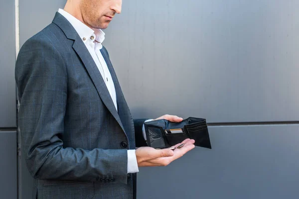 Ausgeschnittene Ansicht eines Geschäftsmannes mit Münzen auf der Handfläche, die leere Brieftasche auf grau strukturiertem Hintergrund — Stockfoto