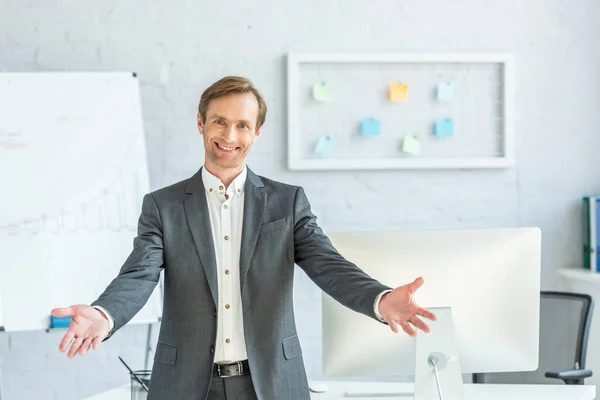 Frontansicht eines glücklichen Geschäftsmannes mit offenen Armen, der in die Kamera blickt, mit verschwommenem Büro im Hintergrund — Stockfoto