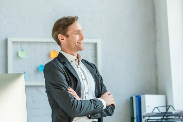 Smiling businessman with crossed arms looking away with blurred office background — Stock Photo